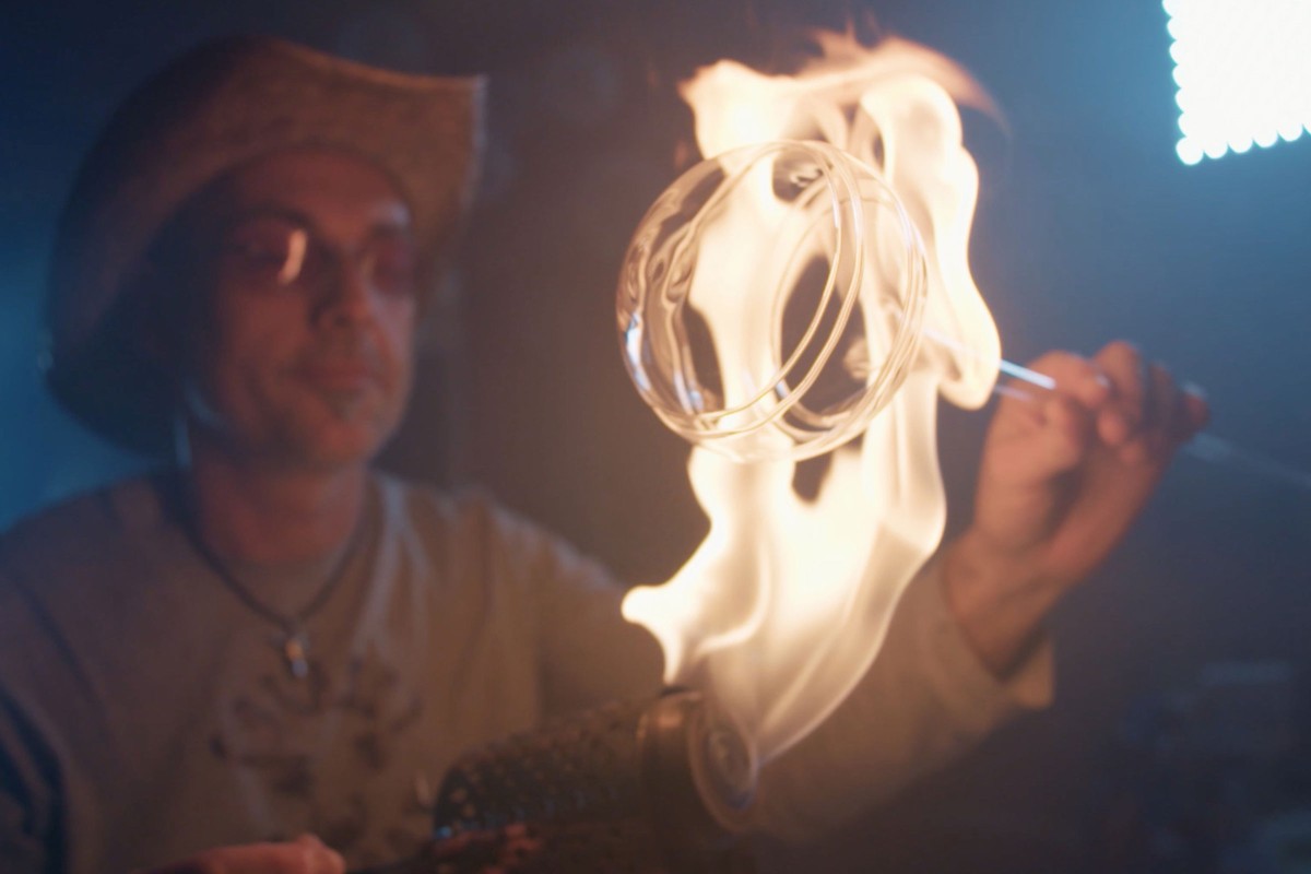 Rolando Vetri hält ein Stück rundes Glas in die Flamme seines Bunsenbrenners, um es zu bearbeiten. 