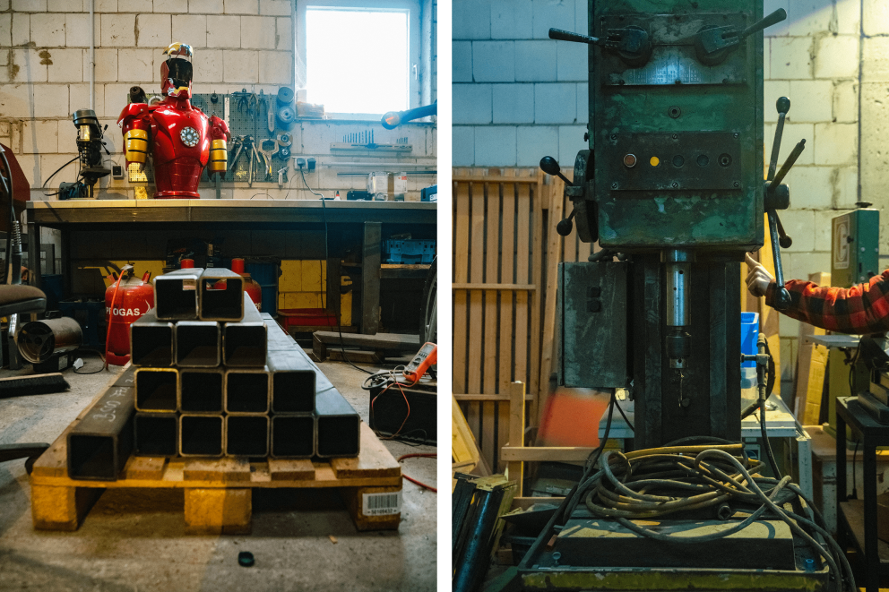 
			Palette mit Stahlträgern, dahinter Werkstatt mit „Iron Man“ Skulptur. Rechts eine alte Standbohrmaschine.

		