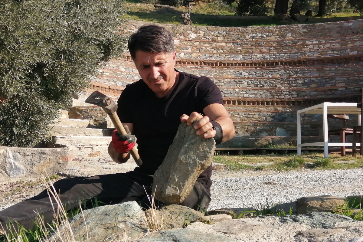 Haydar Zorlu klopft mit dem Hammer einen Stein ab vor seinem selbst gebauten Amphitheater. 
