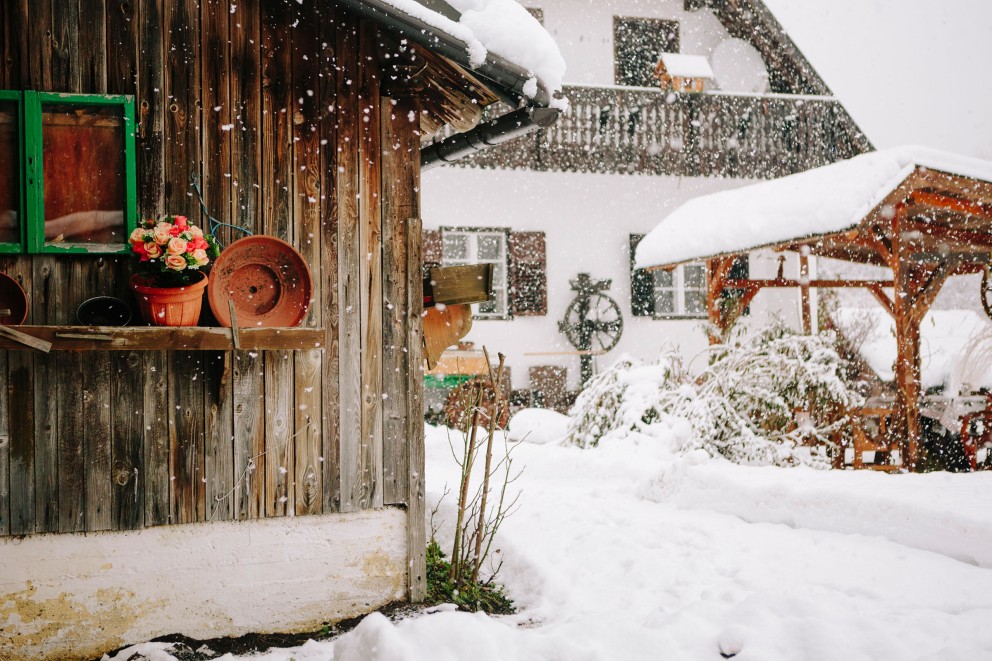 
				Keusche neben einem Bauernhaus im Schneetreiben.

			