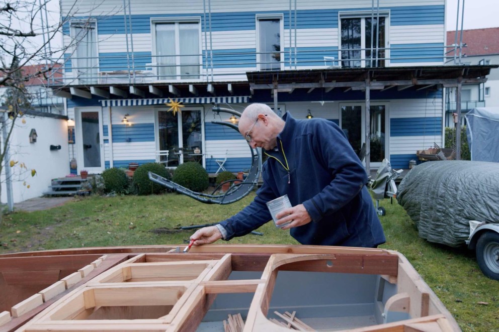 
				Heiner lackiert Teile seines Holzschiffes im Garten.

			