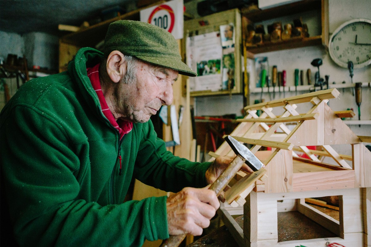 Der 100 jährige Paul Schmiedmaier hämmert ein Stück Holz an den Dachstuhl eines Modells in seiner Werkstatt. 